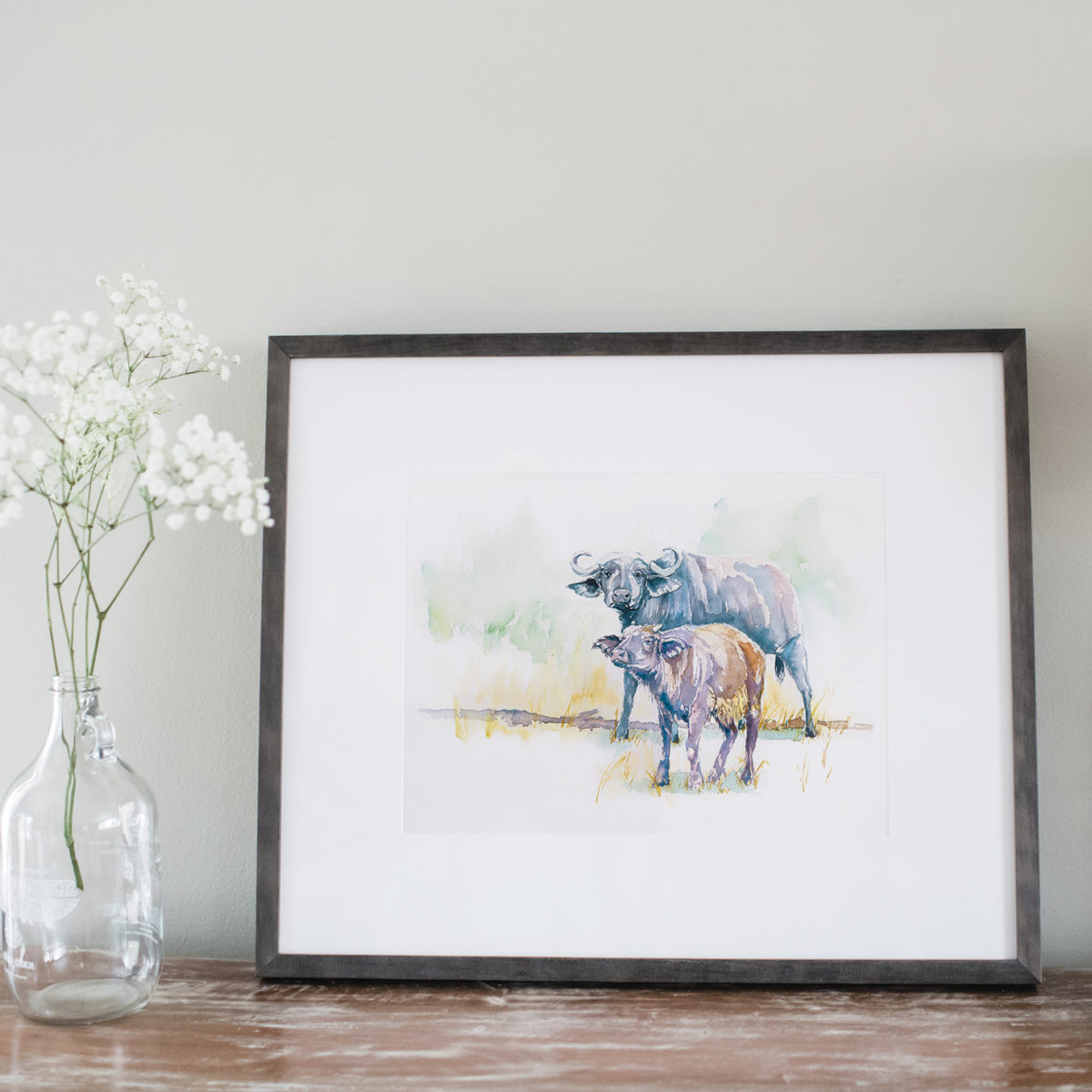 Watercolor of African buffalo in a gray frame next to flowers