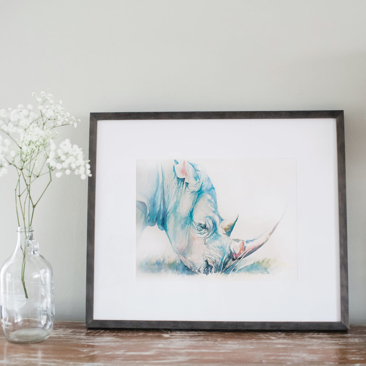 Watercolor of rhino in gray frame and staged with flowers