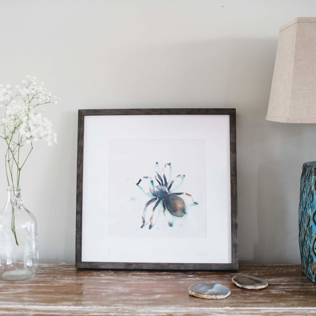 Watercolor of tarantula in gray frame and styled next to flowers and lamp