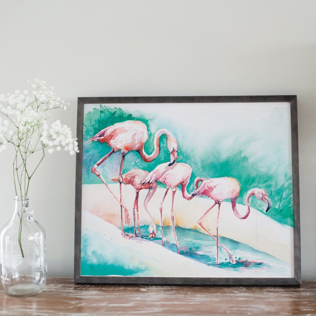 Watercolor of 4 flamingoes in gray frame and next to flowers