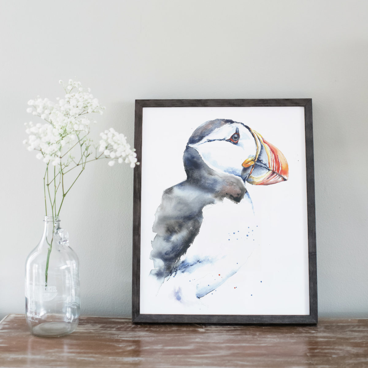 Watercolor of puffin in gray frame with flowers on left